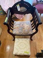 Front view of vintage dark wood chair with floral cushion and matching foot rest on wooden floor.