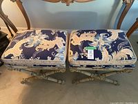 Front view of both stools showing floral upholstered seat cushions and carved wooden frames