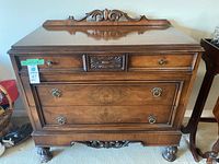 Front view showing two small upper drawers, one center decorative drawer panel, two larger drawers with brass ring handles, carved details on base and top backboard.