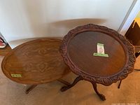 Two unique vintage small wooden side tables, one round with carved edges and claw feet, the other smaller and oval-shaped with natural wood grain.