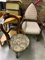 Photo showing the two chairs: a rounded parlour chair with dark floral fabric and a carved wooden frame, and an armchair with pointed back, cream fabric with floral pattern, and spindle wooden legs and arms.
