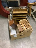 Photo of a cardboard box holding a wood multi-compartment display shelf with slots, two small wood jewelry boxes, and a small wood crate style box.