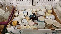 Box of various ceramic egg cups of different sizes and designs including animal-themed and floral styles