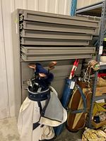 Front view of a large metal file cabinet showing six shallow drawers on top and three deep drawers below with golf bags nearby.
