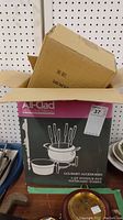 Photo of the All-Clad branded black box with pink label showing the 3 quart fondue pot set and its contents including forks and ceramic insert.