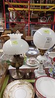 Two vintage milk glass table lamps displayed on a table surrounded by dishware and glassware.