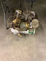 Box of mixed metal and glass light fixtures and lamps including a star-shaped decorative lamp piece, wall sconces with ribbed glass shades, and brass base light fixtures.