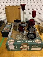 Photo showing five metal display stands, four tall red stemmed glass tea light holders with black metal bases, and a black wooden box behind them.