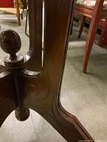 Close-up image of one of the table's decorative carved legs showing swirl patterns and the caster wheel at the base.