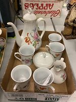 Full tea set including teapot, four cups, cream and sugar bowl arranged in a cardboard box.