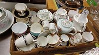 View of the box filled with various teacups, saucers and three teapots including visible damage on Royal Albert teapot.