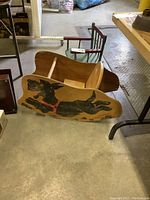 Vintage wooden children's rocking toy with image of running black dog on side, shows veneer peeling and scratches.