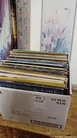Top view of vinyl albums in cardboard box, spines visible, various artists and genres.
