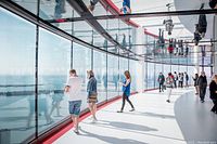 Photo showing visitors inside the CN Tower observation deck with large windows offering panoramic views of the city.