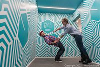 Two people appear to be inside a tilted room with geometric patterned walls, illustrating a visual illusion created in the Museum of Illusions Toronto.