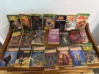 Photo showing full view of 20 fantasy and adventure paperback books arranged on wooden chair, mostly Fighting Fantasy series titles.