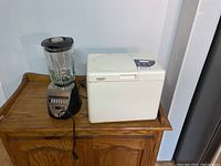 Blender and Citizen bread maker side by side on wooden surface against wall.