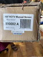 Label showing 100" HDTV Manual Screen, model number 800002 A, made in China.