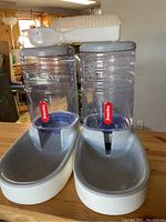 Two Pedigree branded pet food and water dispensers with gray bases and clear reservoirs