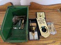 Overview of all components including green plastic container holding metal mounting hardware, keypad door lock panel with push buttons, locking mechanism, and keys.