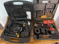 Both cordless drills in their open plastic carrying cases showing drills, chargers, and accessories.