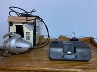 Shark handheld vacuum and MP3 alarm clock radio with cords on wooden surface