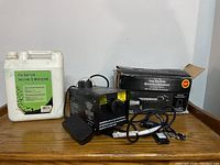 Fog machine, power cord, foot pedal, fog solution container, and original box displayed together