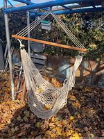 Hammock chair suspended from metal frame outdoors, showing overall condition and rope details.