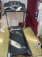 Full view of black and grey Horizon treadmill in unfolded position on a yellow wooden floor near red and white walls.