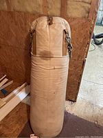 Front view of large beige punching bag with hanging chains, showing visible wear and dirt marks.