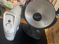 White oil-filled radiator heater next to black oscillating heater on table