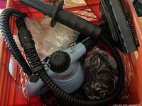 Blue handheld Jiffy steam cleaner with hose and black rectangular brush attachment inside a red plastic crate.
