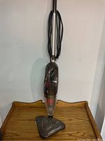 Full view of upright H2O PowerX steam cleaner and vacuum with power cord wrapped on handle, standing on wooden surface.
