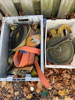 Two bins filled with multiple heavy duty straps of various colors, including orange, yellow, and black. Some straps have metal hooks and ratchets visible.
