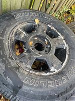 Photo of a Michelin tire mounted on a black metal rim showing wear, dirt, and rust on the rim