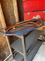 Three frame saws stacked on metal shelving, showing different colored frames and metal blades.
