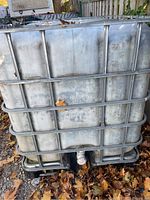 Full view of the rectangular water tote with metal cage showing its size and condition outdoors.