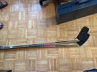 Photo of two wood hockey sticks with PMX 9950 Pro branding on parquet floor, showing the blades taped in black.