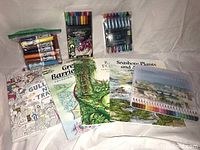 Lot contents showing the front covers of 5 adult coloring books, a 12-pack of colored pencils in a plastic case, a 12-pack of RoseArt Classic Washable markers, and a 12-pack of assorted gel pens.