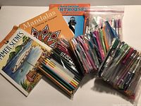 Photo of the three adult coloring books and multiple packs of markers and colored pencils in plastic bags.