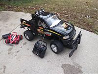 Black 1/6 scale Ford R/C truck with large tires and smaller red and silver R/C car beside it on concrete surface