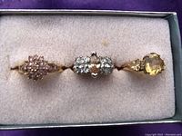 Three gold rings with gemstone settings displayed in a padded jewelry box