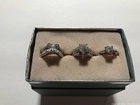 Front view of three silver-tone rings with clear stones arranged in box