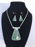 Photo of turquoise inlay trapezoid pendant necklace and matching earrings on black jewelry display.