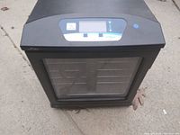 Front view of the black electric towel warmer showing the closed transparent door and digital control panel on top.