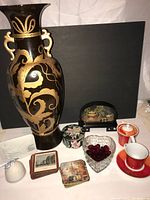 Photo showing the very tall black vase with gold floral designs, Asian-style carved wooden panel decor, two small decorative boxes, heart-shaped glass dish with red stones, and red and white porcelain tea cup set.