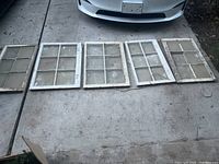 Five antique wooden windows laid on ground in a row beneath a white car, showing overall condition and size differences