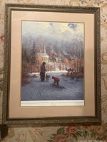 Framed and matted print showing a winter scene with an adult and child near a sled in front of a rural church, with a detailed gold and wood-tone frame and beige matting.