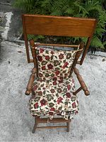 Front view of the antique baby high chair showing floral cushion and wooden arms with turned details.
