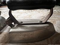 Close-up of antique iron showing worn metal base and riveted handle